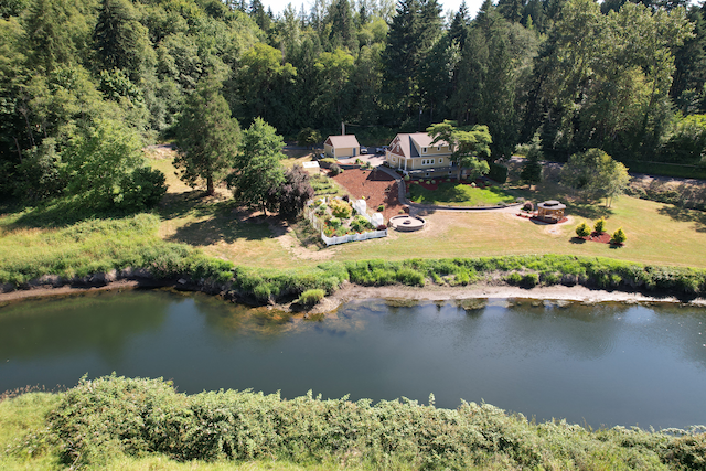 Aerial view hovering above the Cowlitz River dike, looking across the river at a large house and its garden by the riverbank.